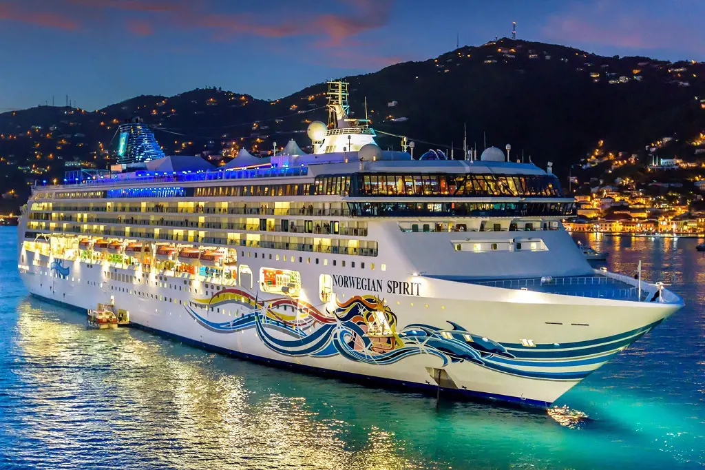 Norwegian Spirit shining on the water under the star and mountain filled with lighten houses